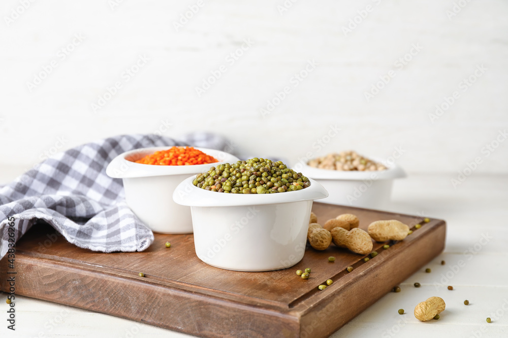 Bowls with different lentils and peanuts on light background