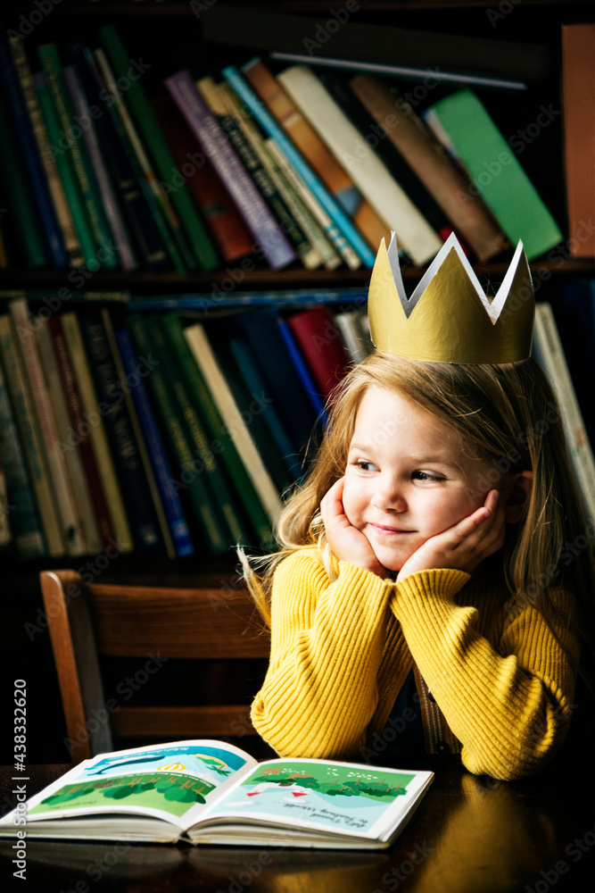 Cute and adorable little girl with paper crown on her head daydreaming