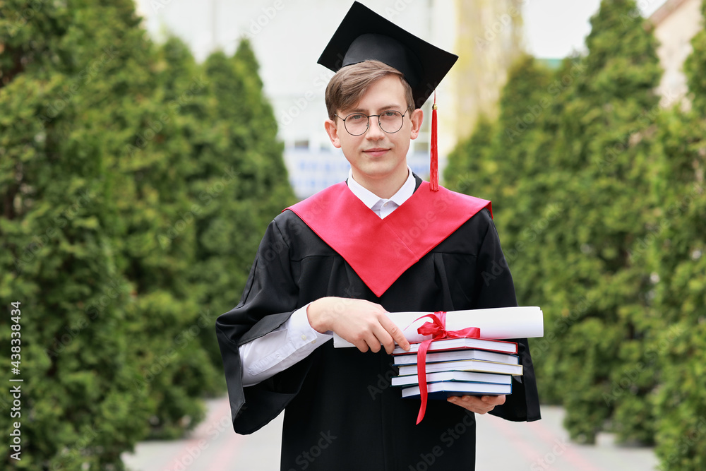 Portrait of male graduating student with books outdoors