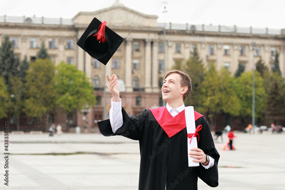 Portrait of male graduating student throwing cap outdoors