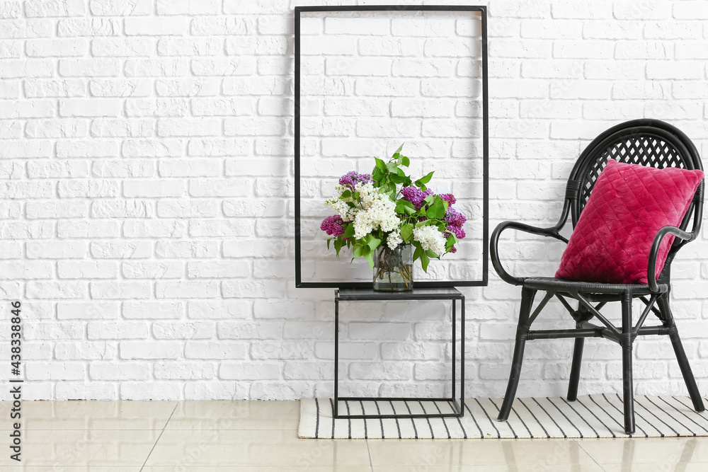 Vase with lilac flowers on table and armchair near brick wall