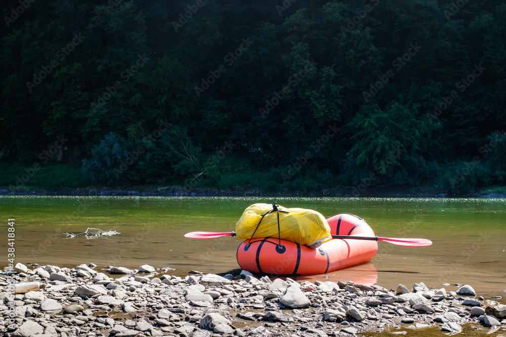 Orange packraft rubber boat with backpack on a river