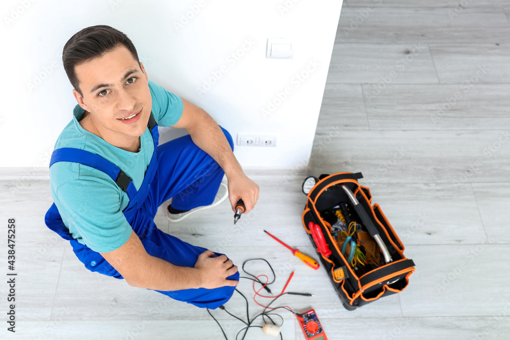 Young electrician repairing socket in room