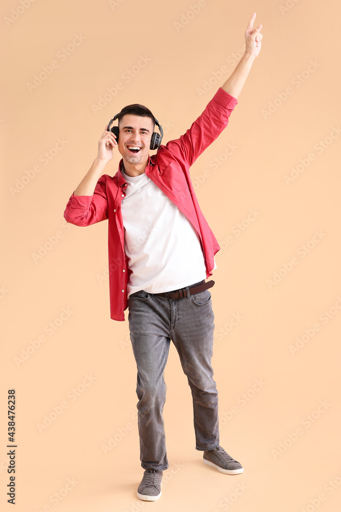 Handsome young man with headphones listening to music on color background