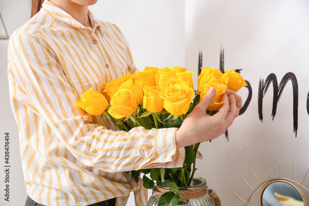 Woman with vase and yellow roses at home