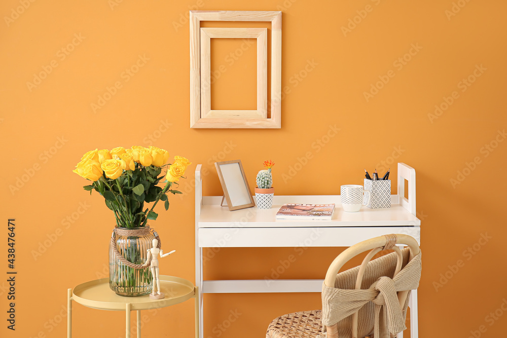 Stylish workplace and vase with yellow roses near color wall