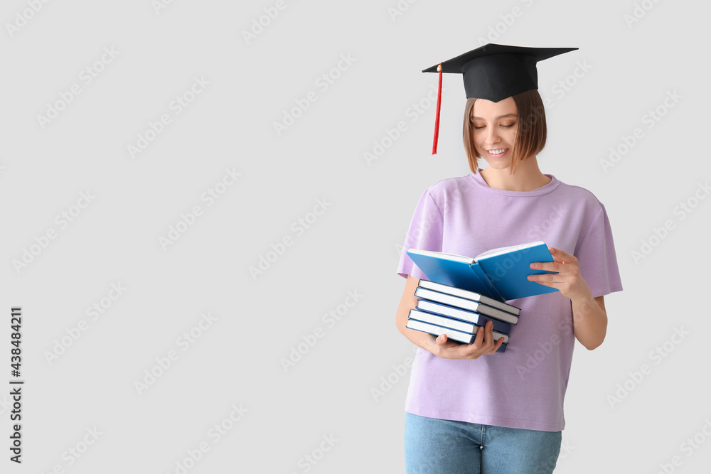 Female graduating student with books on light background