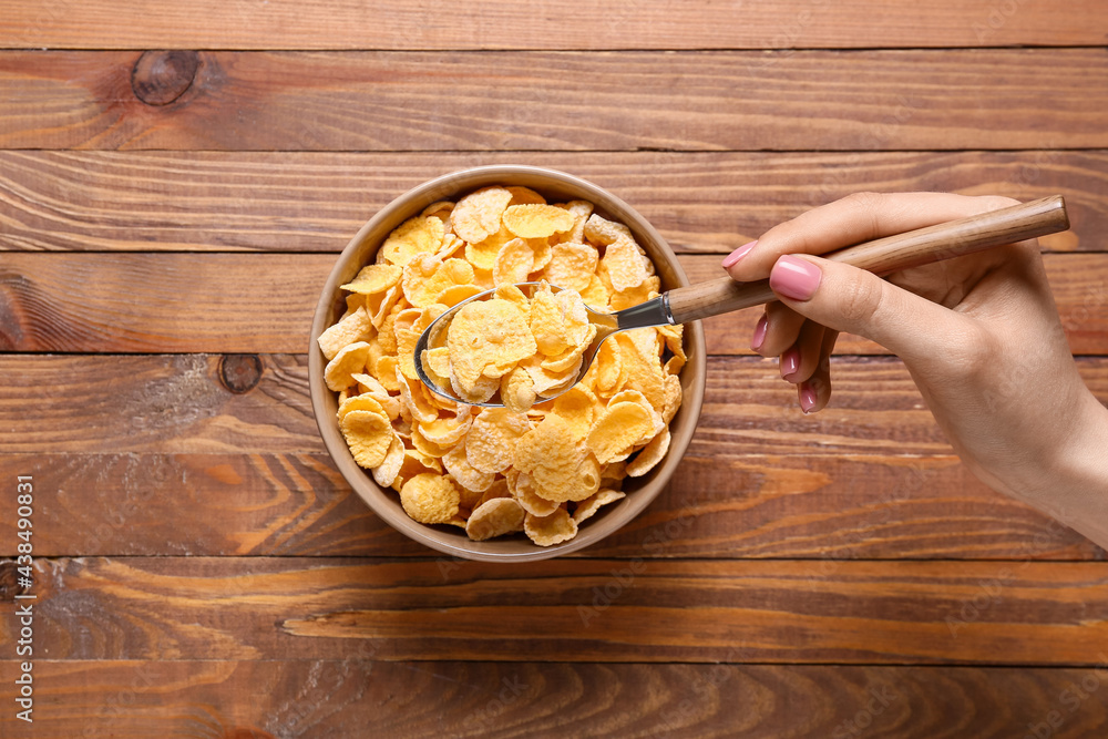 Female hand with bowl of corn flakes on wooden background