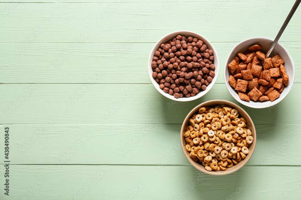 Bowls of different cereals on color wooden background