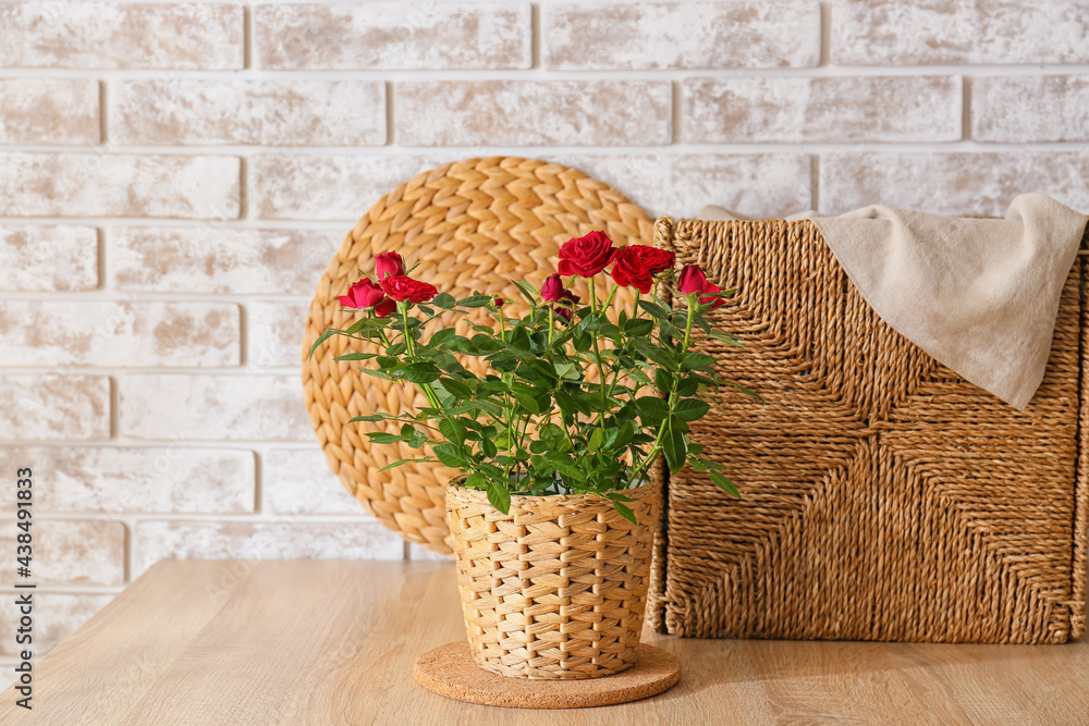 Beautiful red roses in pot on table near brick wall