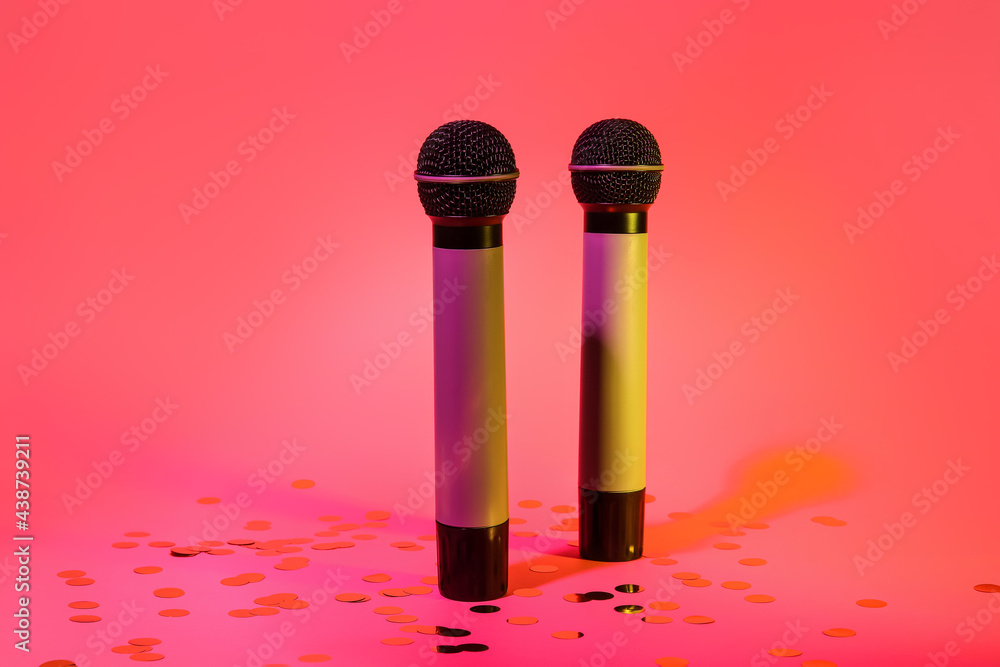 Modern microphones and confetti on color background