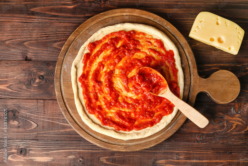 Pizza dough with tasty tomato sauce and cheese on wooden background