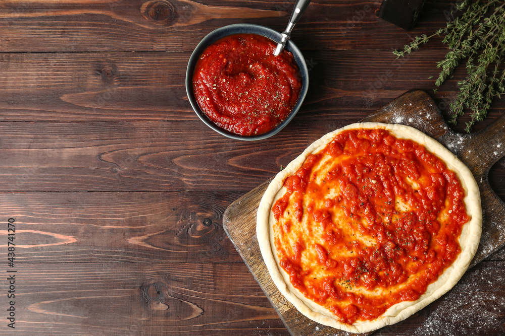 Pizza dough with tasty tomato sauce on wooden background