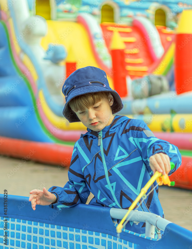 8 year old boy outdoors is fishing in the paddling pool.