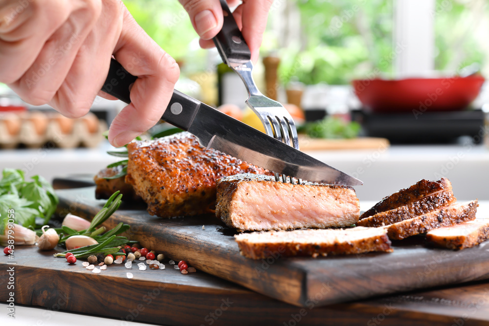 Hand slicing grilled pork steaks with spices on wooden cutting board in the kitchen