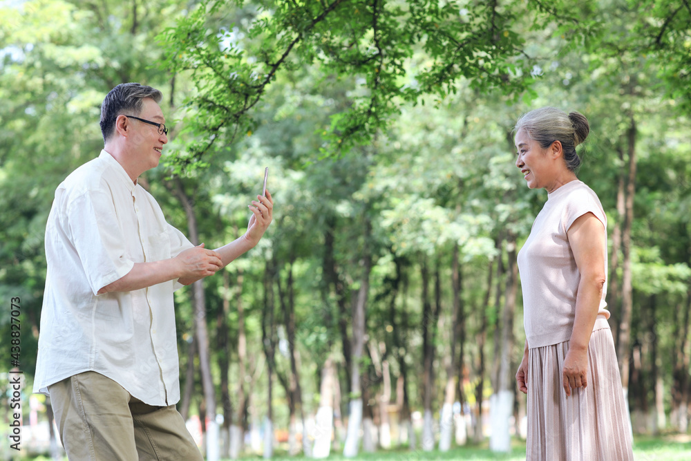 Happy old couple taking photos with mobile phone in the park