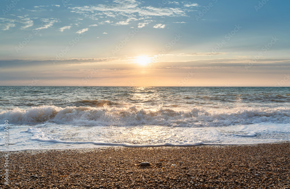 Green blue sea splashing waves backlit by setting sun in front of beautiful sunset sky background. T