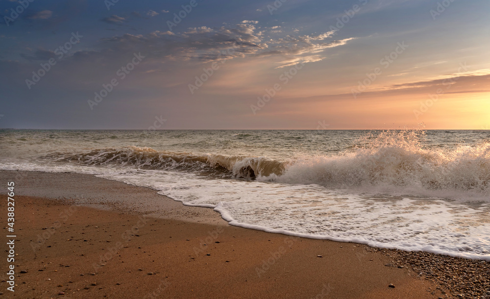 Green blue sea splashing waves backlit by setting sun in front of beautiful sunset sky background. T