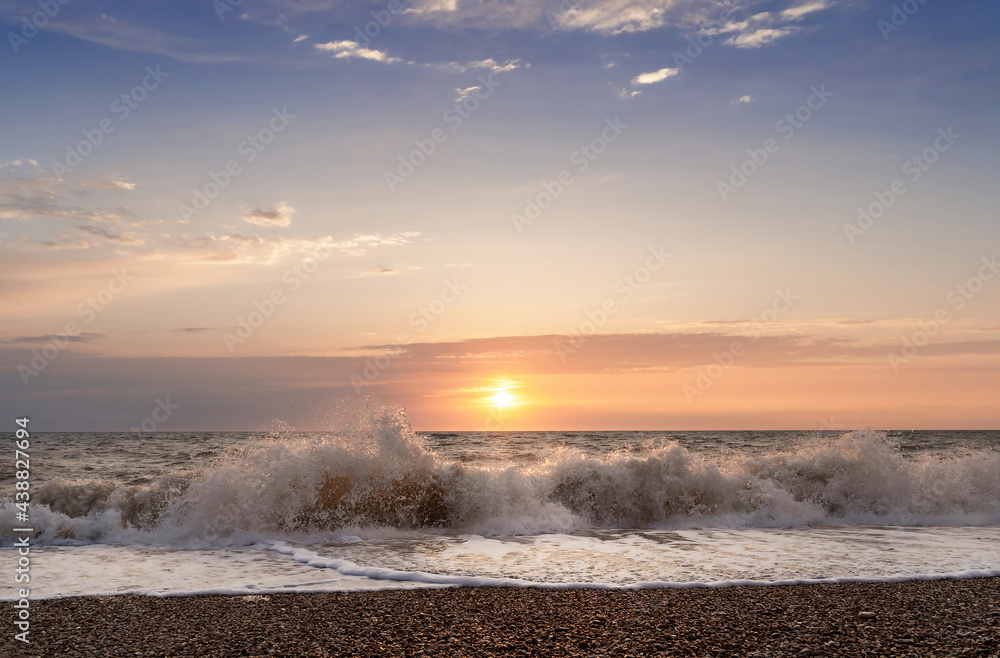 Green blue sea splashing waves backlit by setting sun in front of beautiful sunset sky background. T