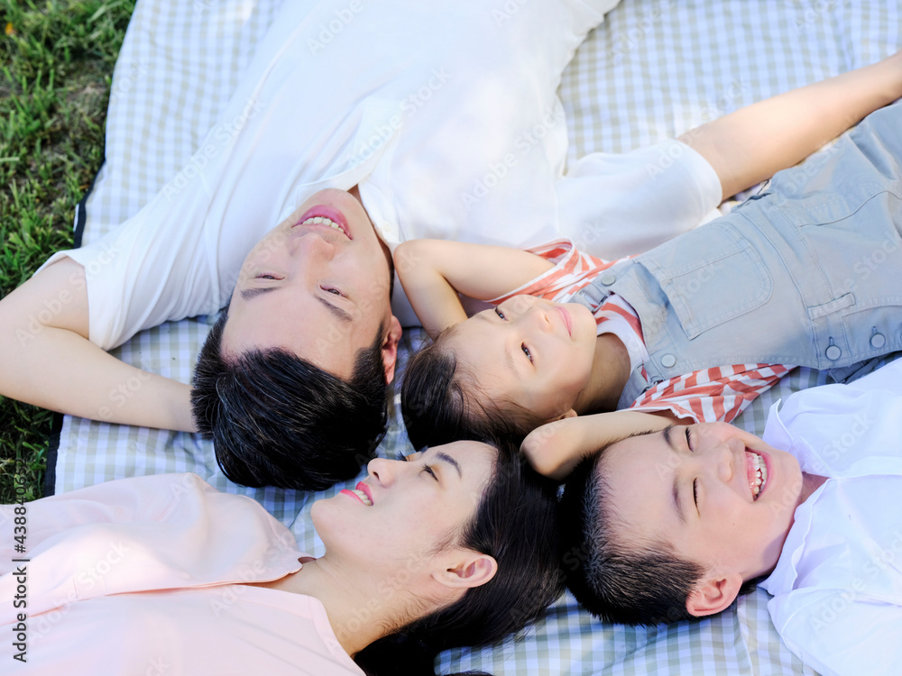 Happy family of four lie on the park grass to rest