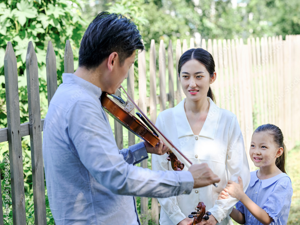 Happy family of three playing violin in the park