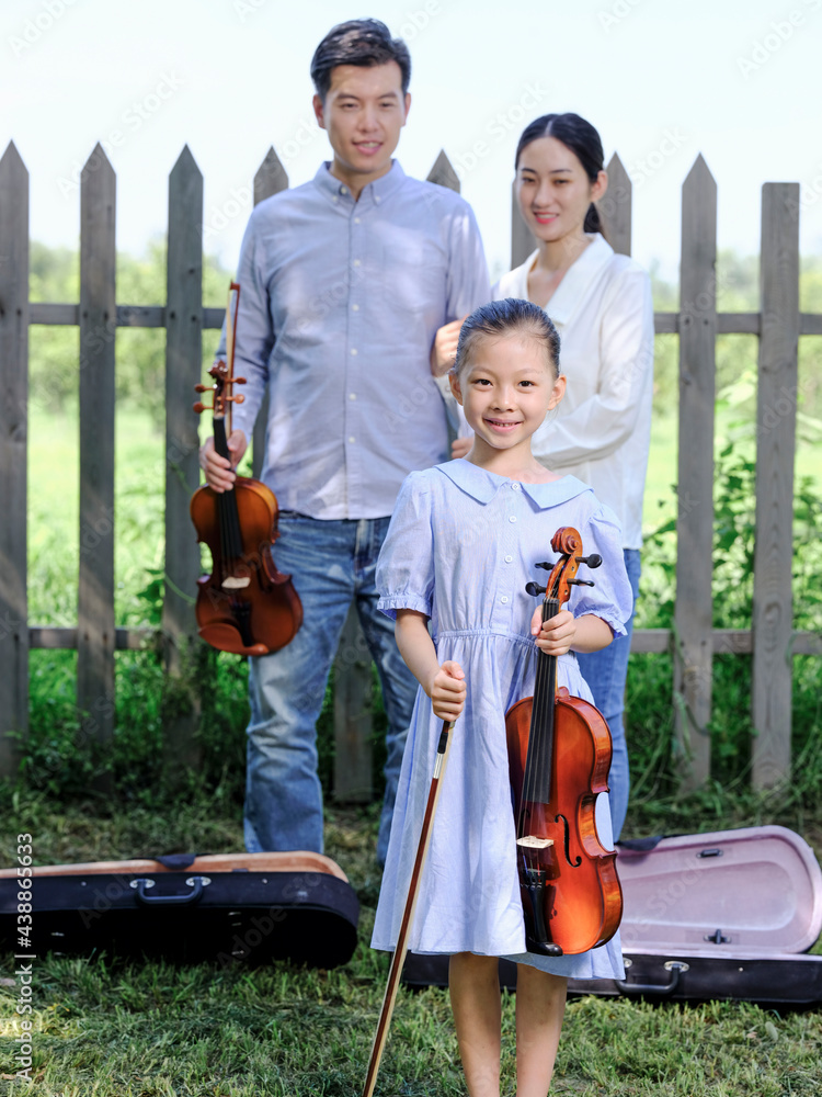 Happy family of three playing violin in the park