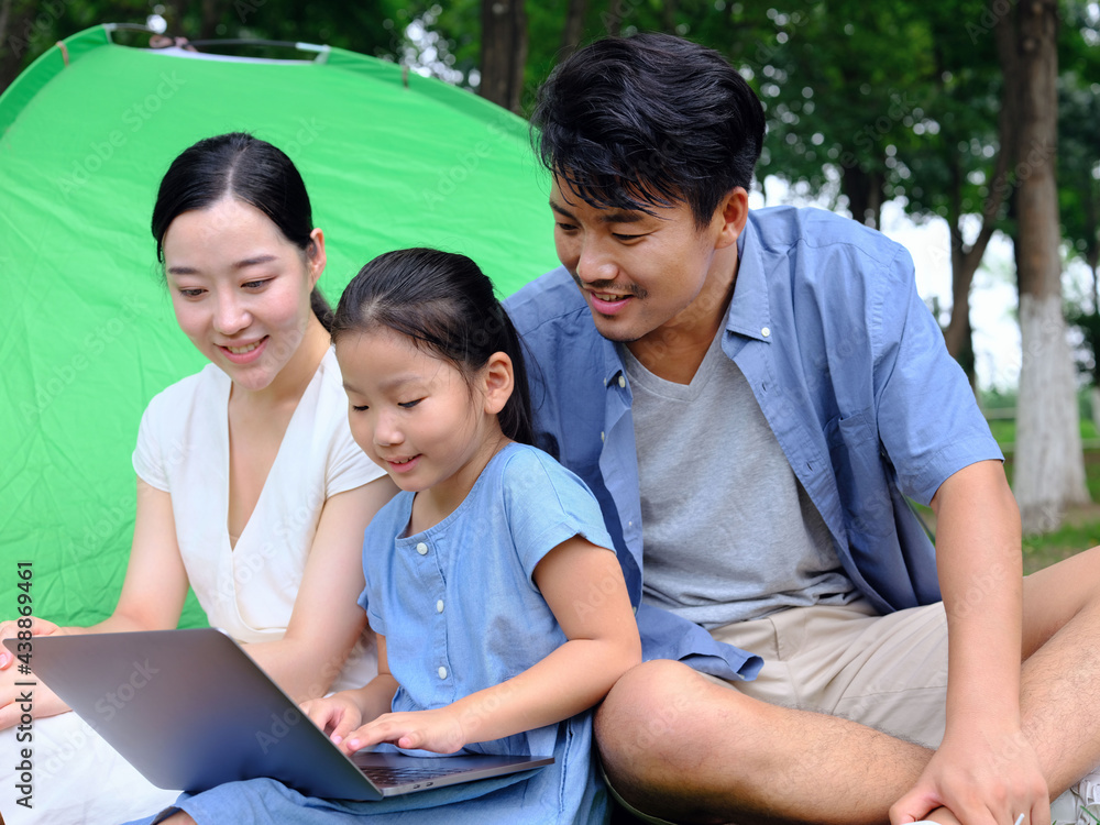 Happy family of three use computer to surf the Internet outdoors