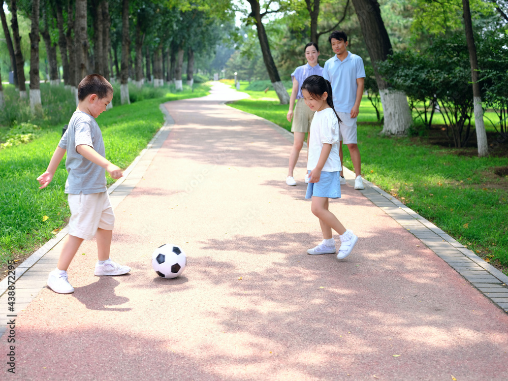 Happy family of four playing football in the park