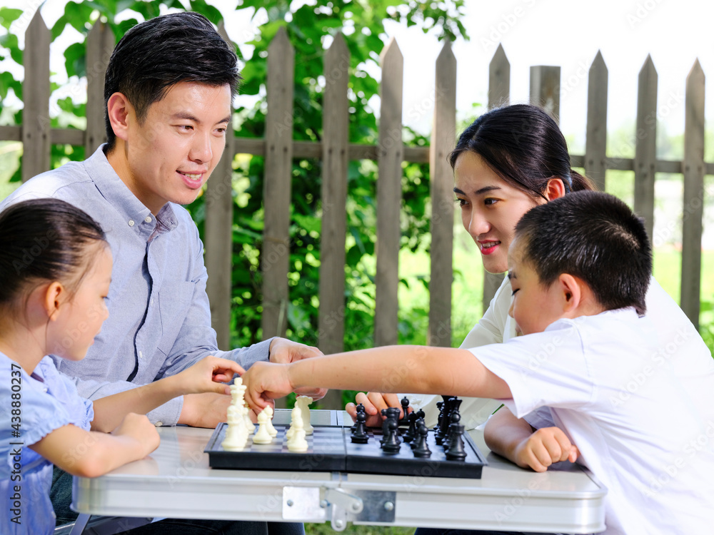 Happy family of four playing chess in the park