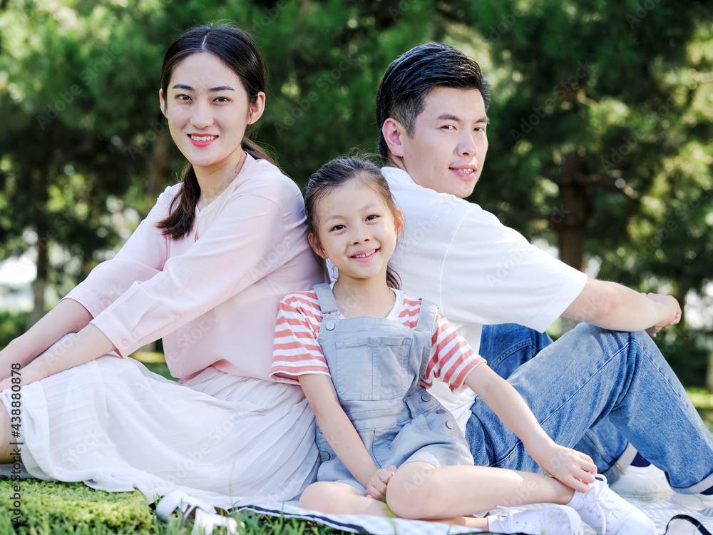 Happy family of three sitting on the park grass