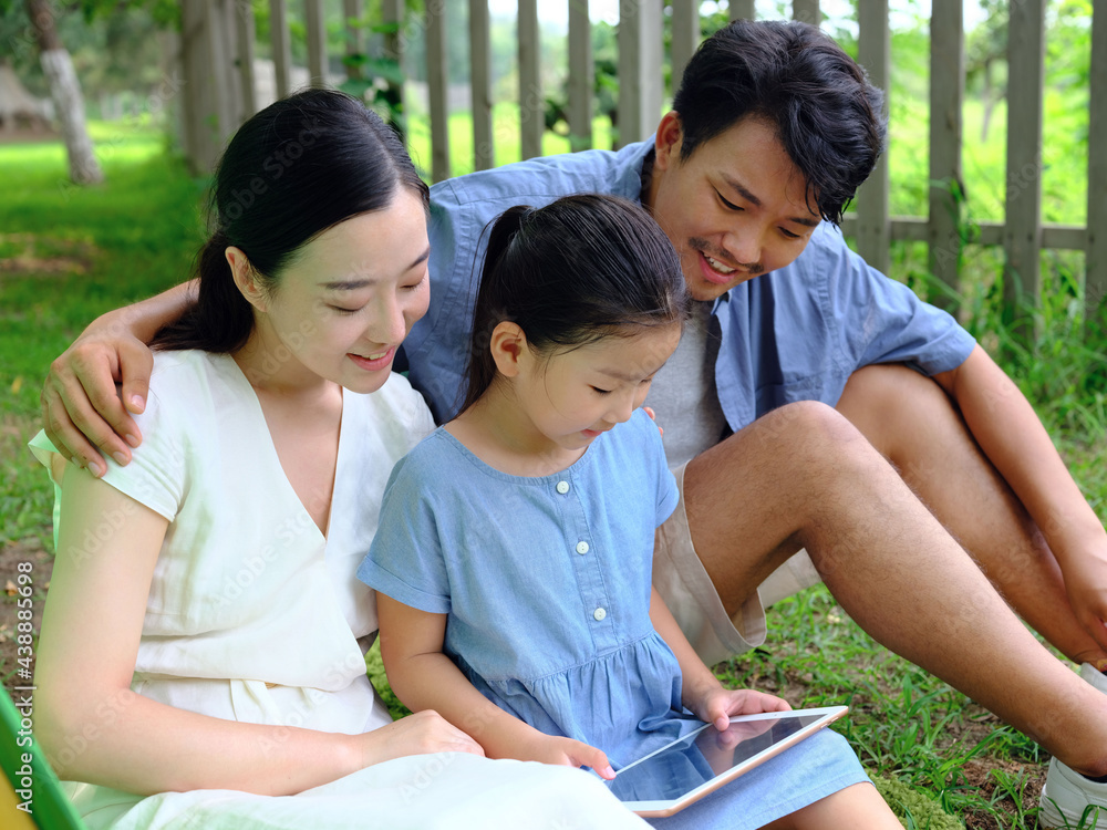 Happy family of three uses tablet computer outdoors