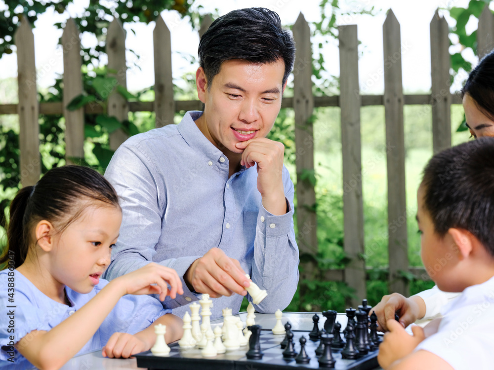 Happy family of four playing chess in the park