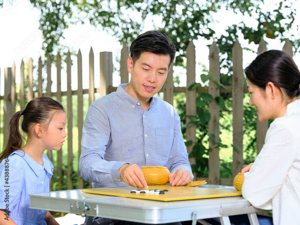 Happy family of three playing chess in the park