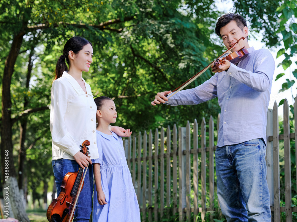 Happy family of three playing violin in the park