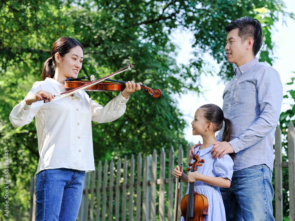 Happy family of three playing violin in the park