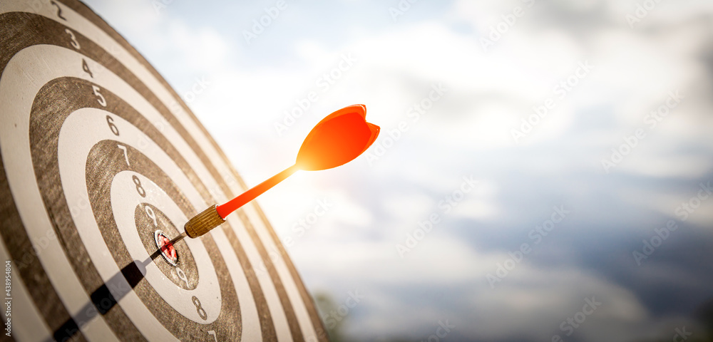 Close up shot red darts arrows in the target  of dartboard center on dark blue sky background. Busin