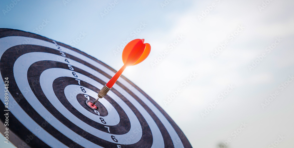 Close up shot red darts arrows in the target  of dartboard center on dark blue sky background. Busin