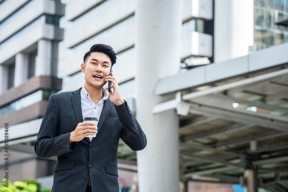 Asian businessman talking on the phone while walking to office in city	
