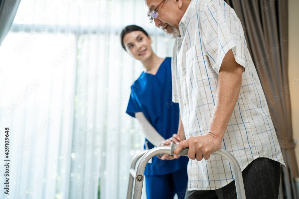 Asian female therapist helping senior male patient to practice walking	