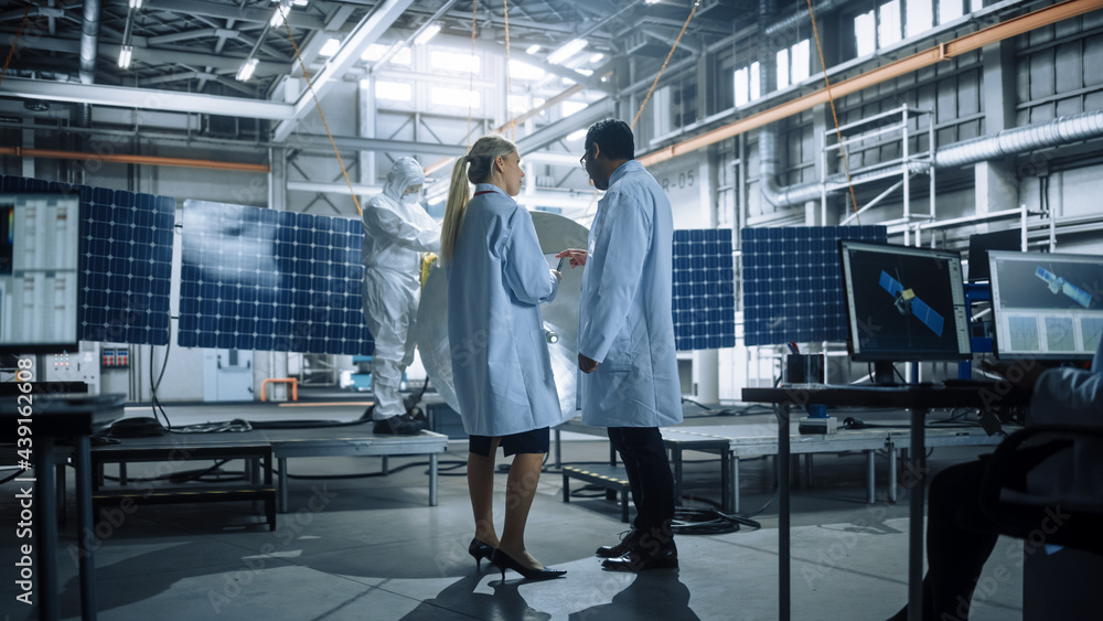 Two Engineers Talk, Use Tablet Computer while Working on Satellite Construction. Aerospace Agency Ma