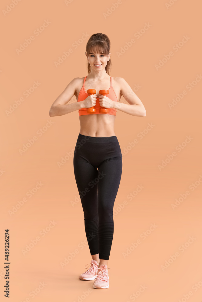 Sporty young woman with dumbbells on color background