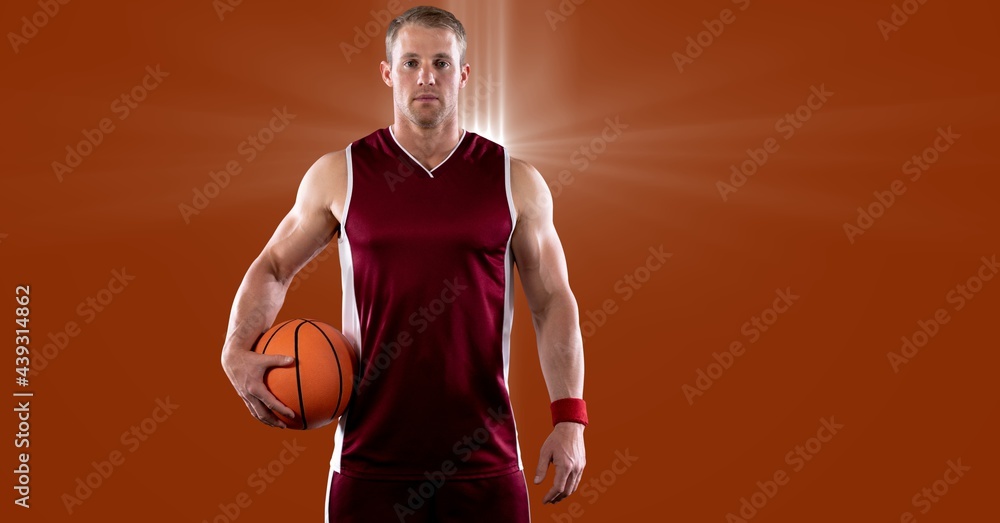 Portrait of caucasian male basketball player holding basketball against spot of light in background