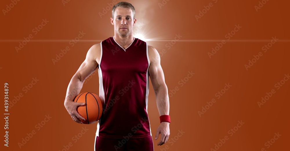 Portrait of caucasian male basketball player holding basketball against spot of light in background