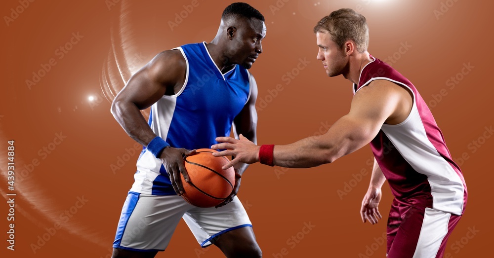 Two diverse male basketball players playing basketball against spot of light in background