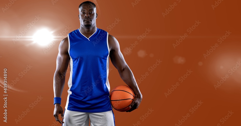 African american male basketball player holding basketball against spot of light in background