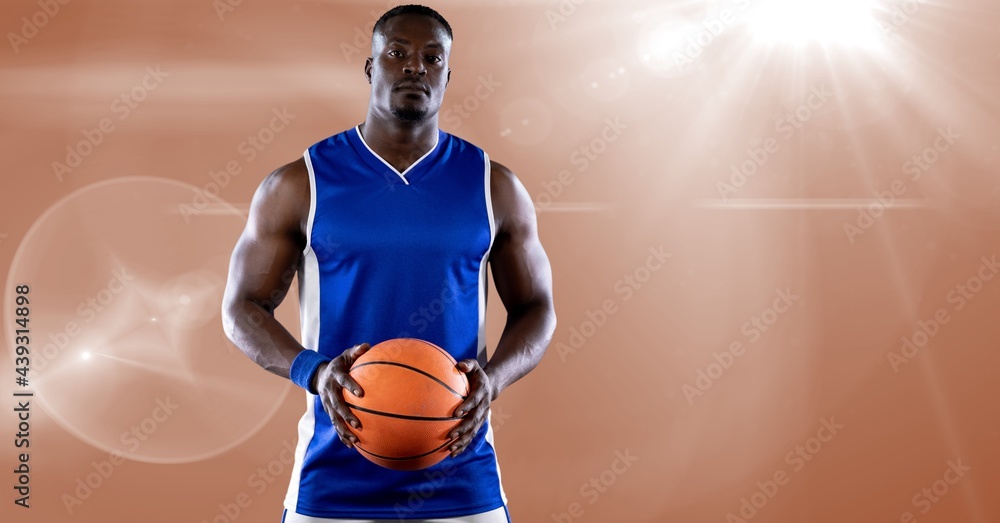 African american male basketball player holding basketball against spot of light in background