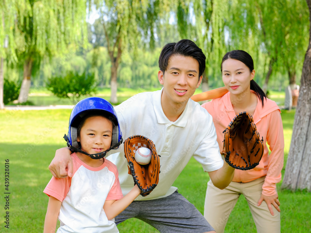 Happy family of three playing baseball in the park