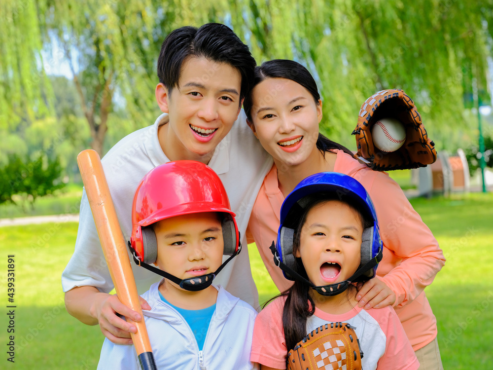 Happy family of four playing baseball in the park