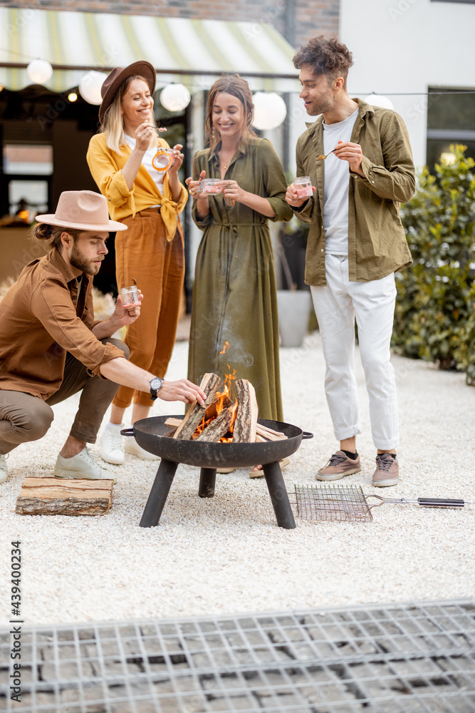 Group of young friends hang out by a fireplace, preparing for grilling at the backyard. Barbecue in 