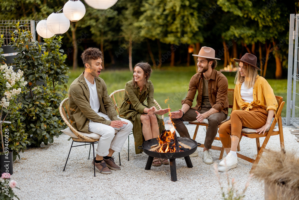 Friends sitting by a fireplace, having great summertime at backyard near the forest. Barbecue in clo